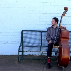Brendan Keller-Tuberg with his upright bass sitting on a bench
